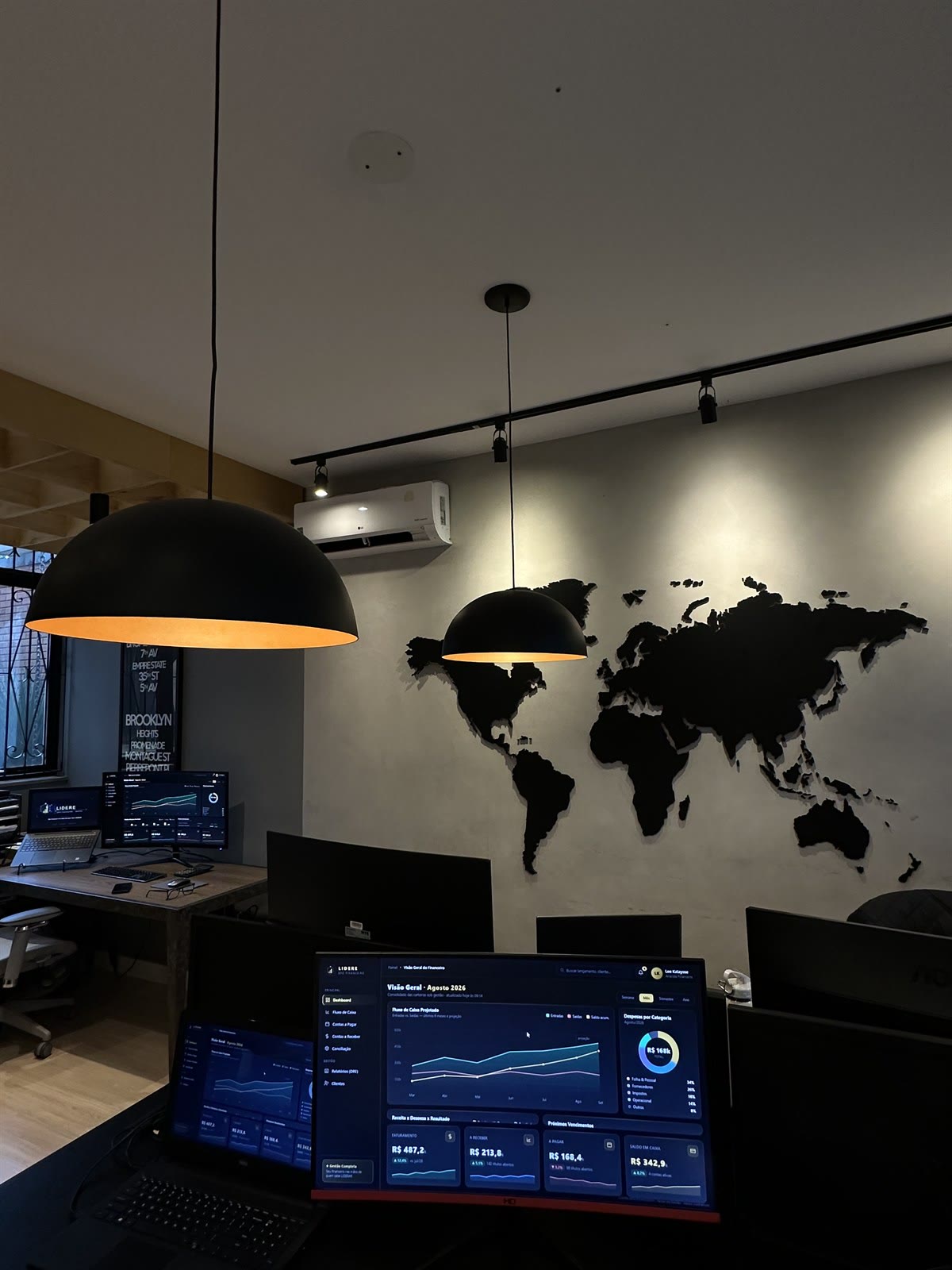Sala de operação da Lidere com painéis financeiros e mapa-múndi na parede